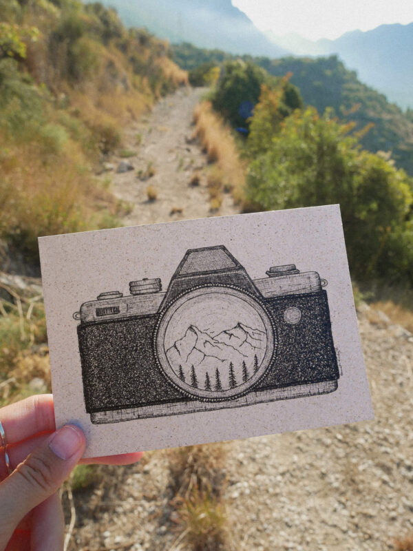Karte aus Graspapier mit gezeichneter Kamera und Berglandschaft in der Linse