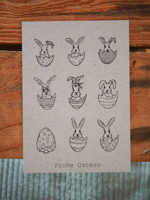 Osterkarte mit neun kleinen Hasen, die in Eierschalen sitzen und dem Text "Frohe Ostern"