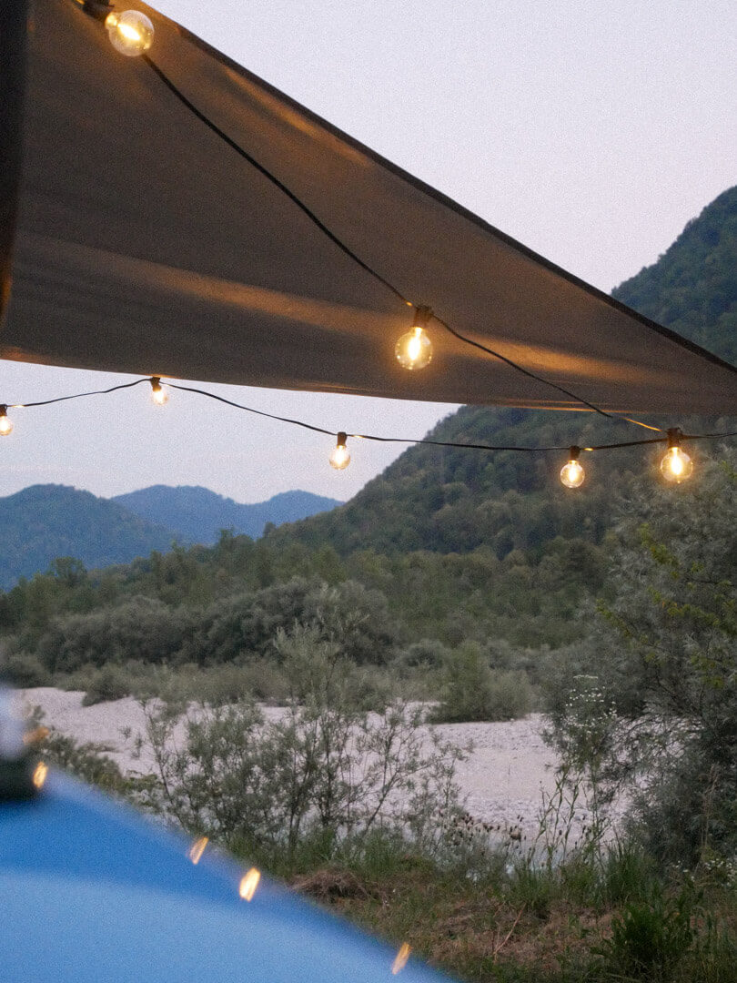 Campingszene: Markise mit Lichterkette und Blick auf den Fluss